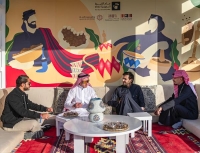 أشخاص يشربون قهوة سعودية خلفهم الهوية البصرية لعام القهوة السعودية- اليوم