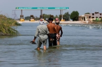 باكستانيون يسيرون وسط مياه الفيضان غير المسبوق بالبلاد (رويترز)