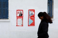 شابة تونسية تسير وعلى يمينها ملصقات لمرشحين بالبرلمان- رويترز