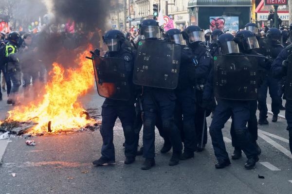 ضباط إنفاذ القانون يسيرون بجوار حريق خلال مظاهرة ضد خطة الحكومة الفرنسية لإصلاح نظام التقاعد في باريس- رويترز 