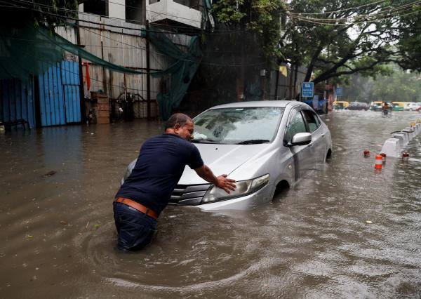 رجل يدفع سيارة في شارع غمرته المياه بعد هطول أمطار غزيرة في نيودلهي - رويترز