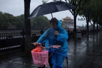 امرأة تحمل مظلة أثناء مرورها بالدراجة بأحد ضواحي بكين - رويترز