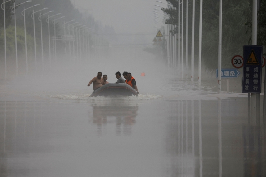 خاص يركبون قاربًا عبر طريق غمرته المياه بعد هطول الأمطار والفيضانات - رويترز