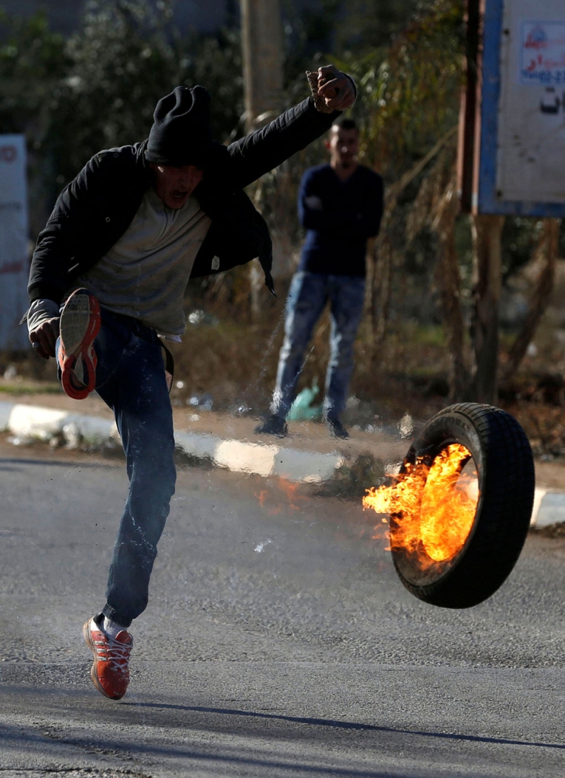متظاهر فلسطيني يركل إطارا مشتعلا خلال اشتباكات مع قوات الاحتلال في نابلس (رويترز)