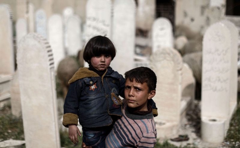 طفلان سوريان تحيط بهما شواهد قبور لشهداء قصف الأسد على دوما (أ ف ب)