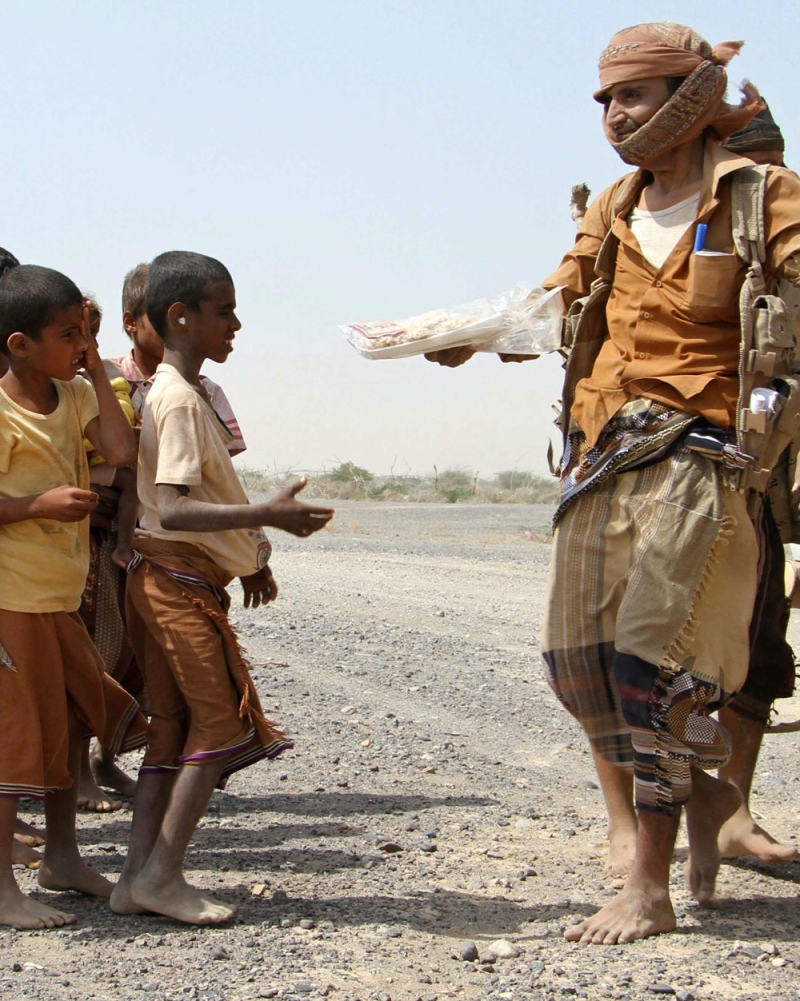 جندي بالمقاومة اليمنية يتقاسم وجبته مع أطفال في طريق المخا (أ ف ب)