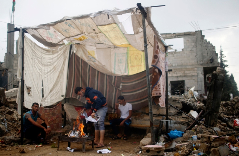 فلسطينيون يقيمون خيمة قرب منزلهم المدمر جراء العدوان الإسرائيلي (رويترز) 