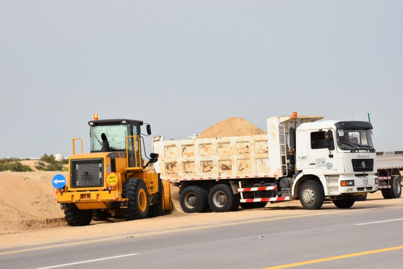 آليات النقل ترفع الرمال عن جانب الطريق (تصوير: محمد العويس) 