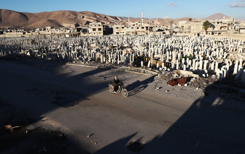 سوري على دراجته النارية يعبر بجوار مقبرة في بلدة للمعارضة بـ«دوما» 