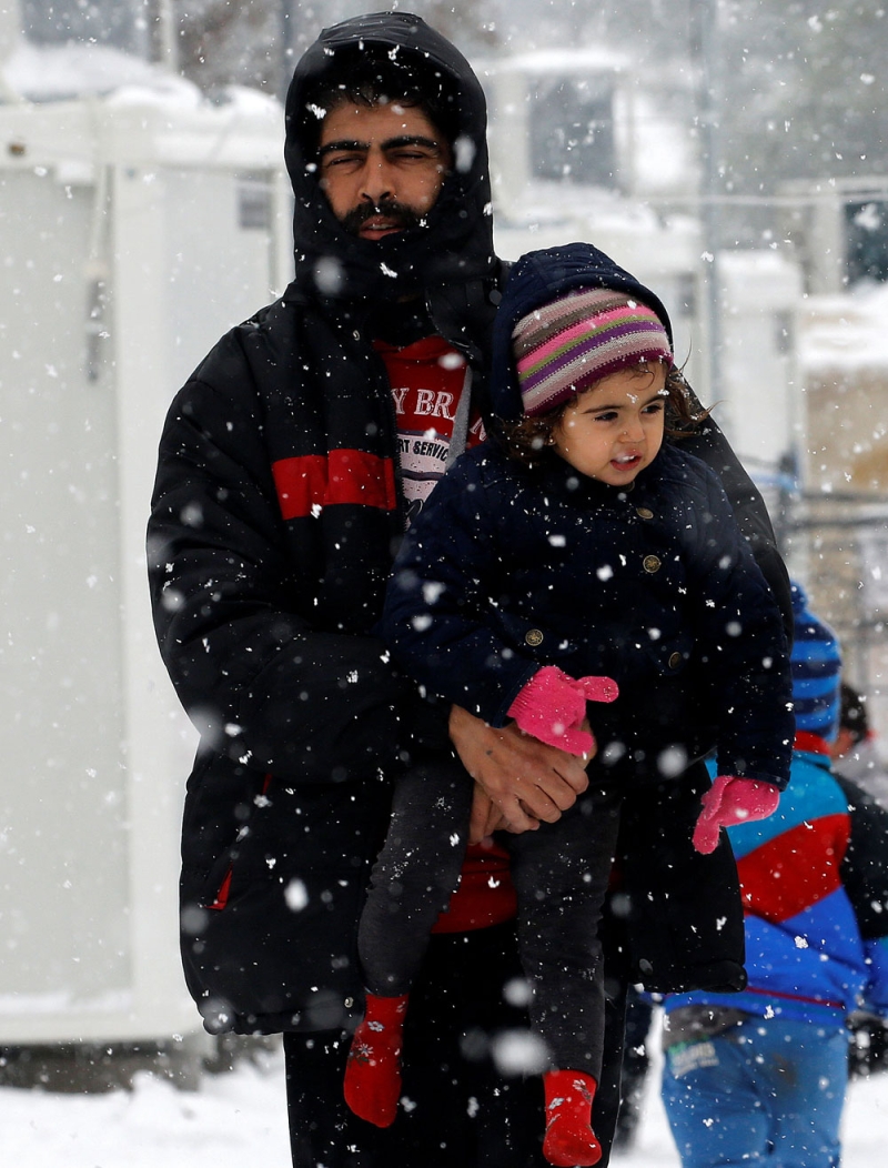 مهاجر سوري يحمل طفله في معسكر للاجئين شمال العاصمة اليونانية