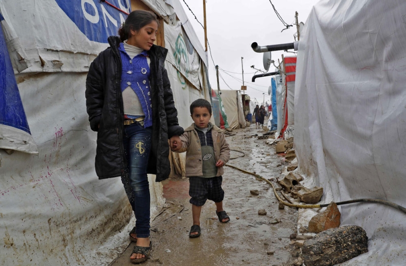 أطفال سوريون يمشون في زقاق بمخيم للاجئين بسهل البقاع في لبنان (أ.ف.ب)