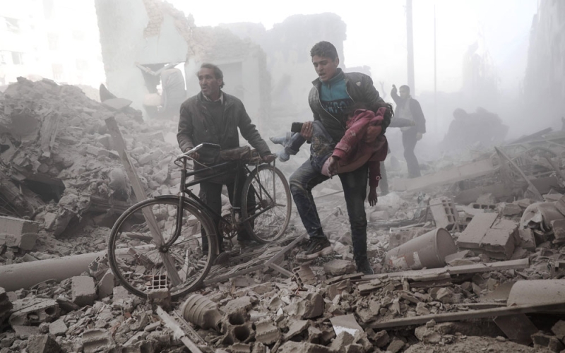 شاب سوري يحمل طفلة مصابة بعد غارة لطائرات الأسد الحربية على دوما (أ.ف.ب)