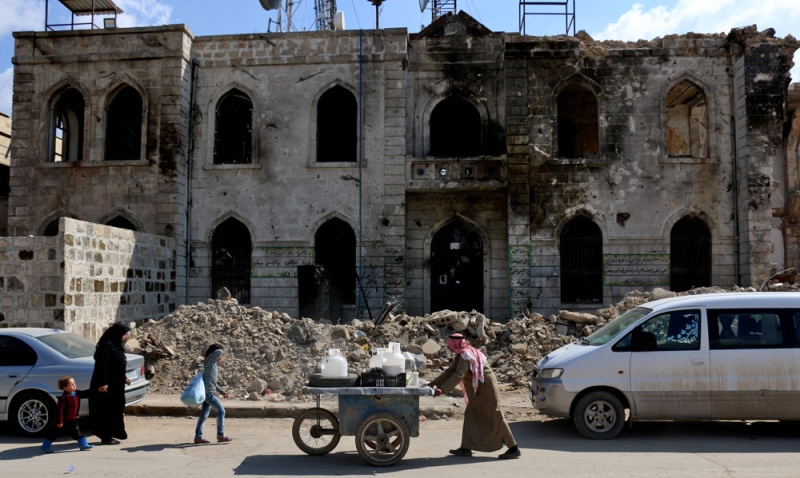 سوري يدفع عربة أمام مبنى مدمر في بلد أعزاز بمحافظة حلب (أ ف ب)
