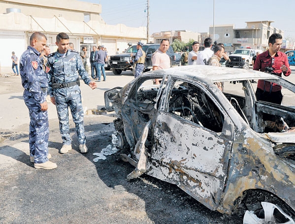  رجلا أمن عراقيان أمام سيارة محترقة جراء انفجار دراجة نارية مفخخة في كركوك 