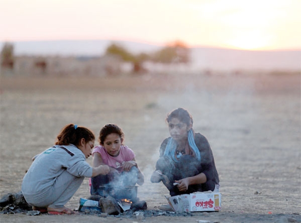 فتاة من اللاجئين السوريين تطبخ طعاما وأشقاؤها يلهون حولها جنوب شرق سوروس في مقاطعة سانليورفا جنوب تركيا