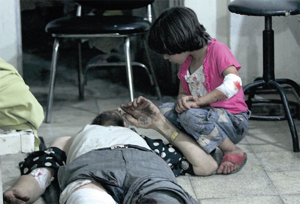 طفلة تجلس بجانب والدها المصاب داخل المستشفى الميداني في دوما