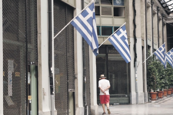  رجل يمشي وسط اثينا أمام المحلات التجارية المغلقة 