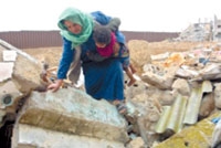 فلسطينية تحمل طفلها على ركام بيتها المدمر في غزة