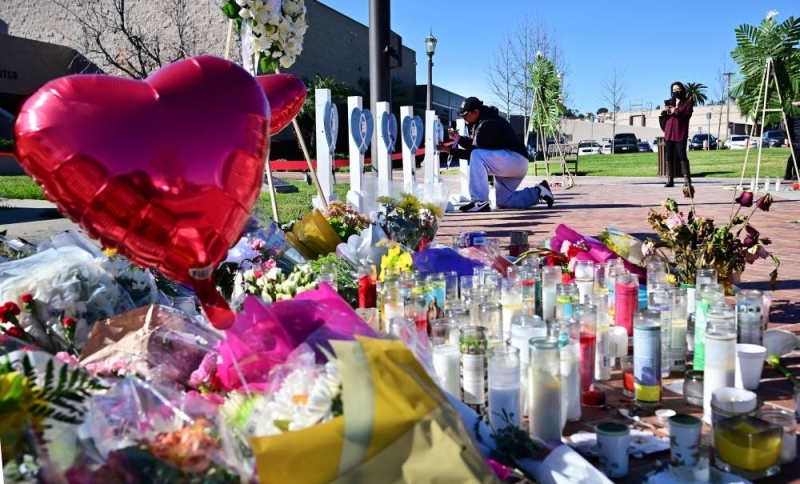 A man writes a note on one of 11 crosses displayed for victims of the January 21 shooting outside City Hall in Monterey Park, California, on January 24, 2023. In between, a makeshift memorial decorated with flowers, candles and balloons. 