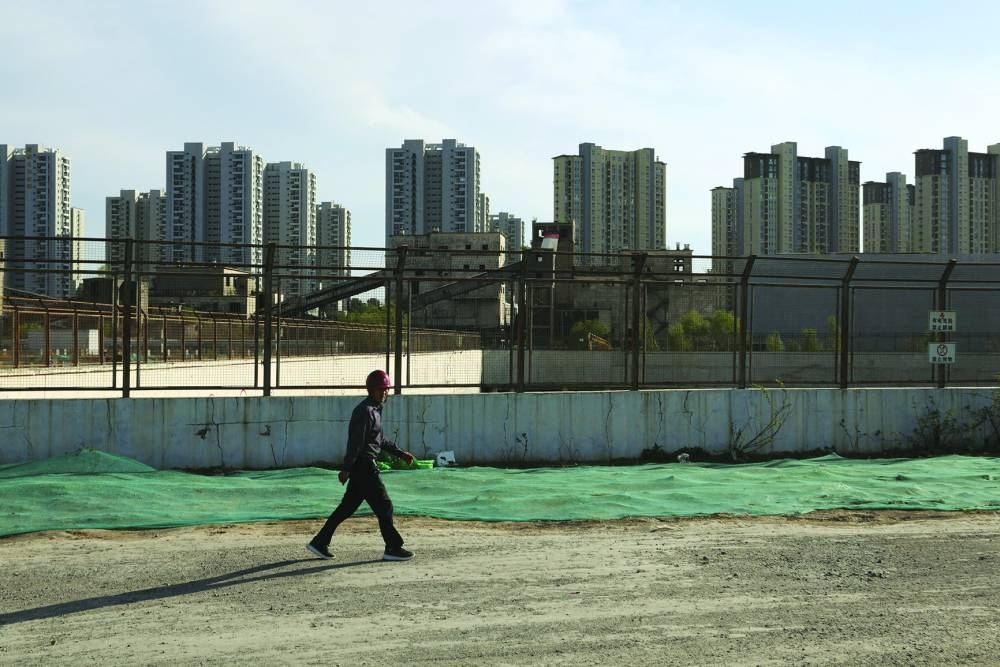 A worker walks past a construction site near residential buildings in Beijing.
