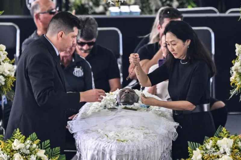 The wife of late Brazilian football legend Pele, Marcia Aoki (R), places a rosary on his coffin during his wake at the Urbano Caldeira stadium in Santos, Sao Paulo, Brazil. AFP