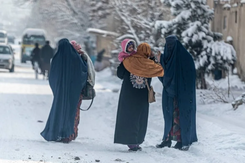 Burqa-clad women carry children as they walk along a snow laden street in Kabul on January 23. AFP
