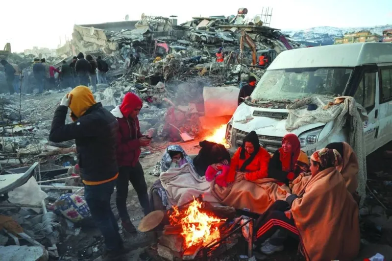 Survivors gather next to a bonfire outside collapsed buildings in Kahramanmaras, Turkiye Wednesday. AFP