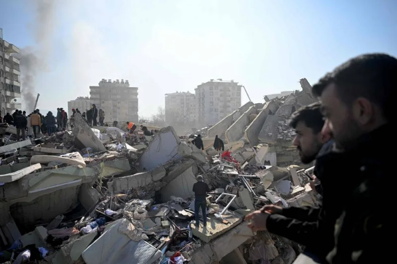 Families of victims stand as rescue officials search among the rubble of collapsed buildings in Kahramanmaras (AFP)
