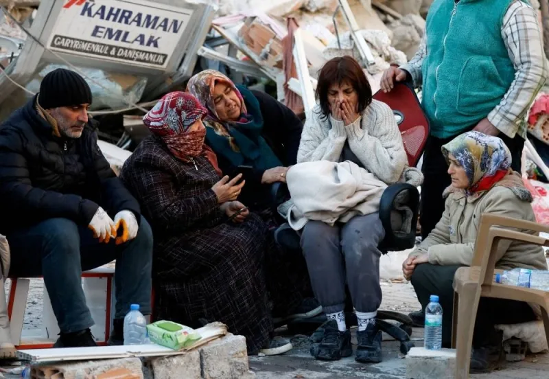 People sit next to rubble at the site of a collapsed building in the aftermath of a deadly earthquake, in Kirikhan, Turkey, Thursday. REUTERS