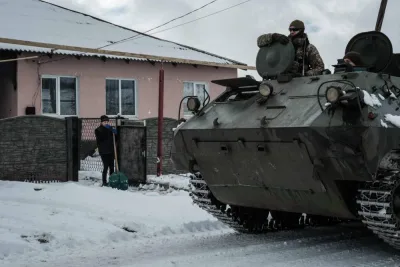 A woman stops shovelling snow as a Ukrainian armoured personnel carrier (APC) passes near Chasiv Yar. (AFP)