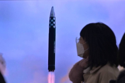 A woman walks past a television showing a news broadcast with file footage of a North Korean missile test, at a railway station in Seoul on February 18.