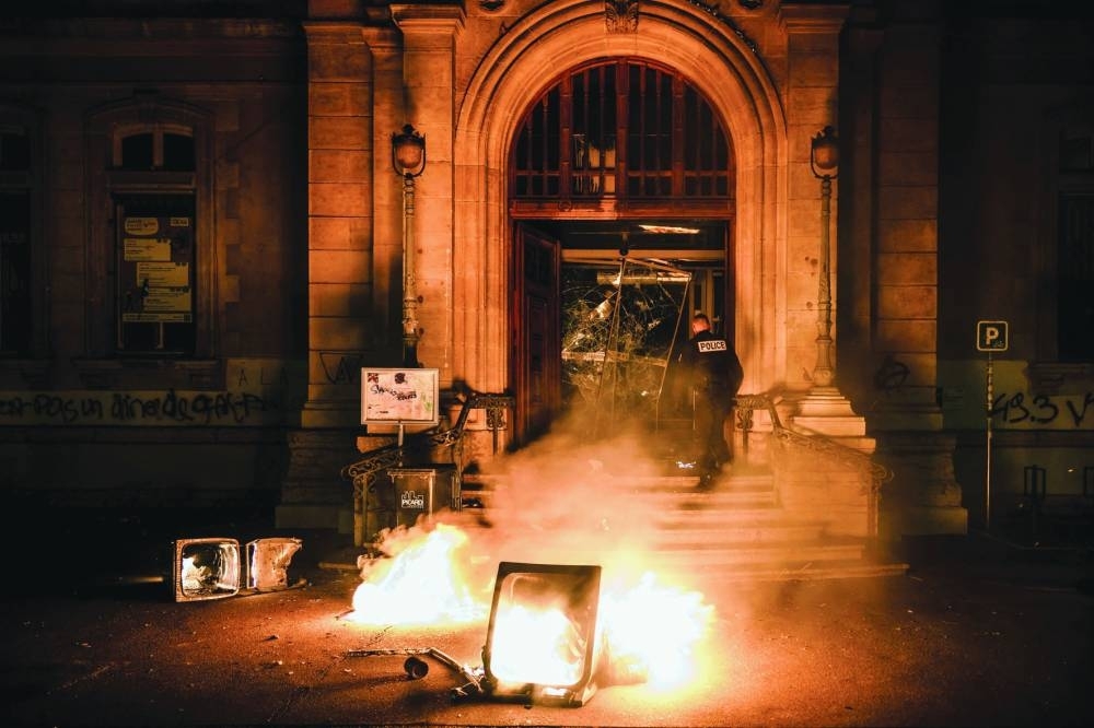 A police officer attempts to extinguish flames at the entrance of the town hall of the 4th arrondissement (district) of Lyon, which was vandalised during riots following a demonstration after the French government pushed a pensions reform using the article 49.3 of the constitution.