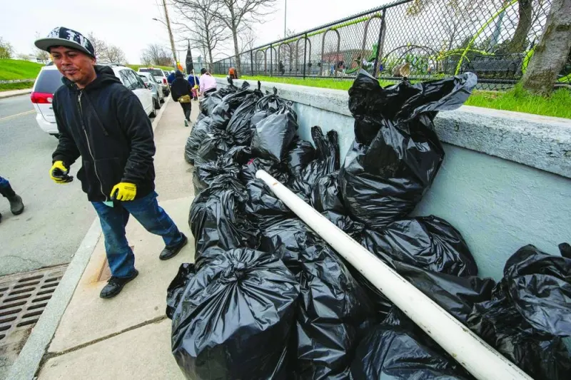 A person walks by bags filled with trash picked up around a waterfront area along the Mystic River on Earth Day in Boston.