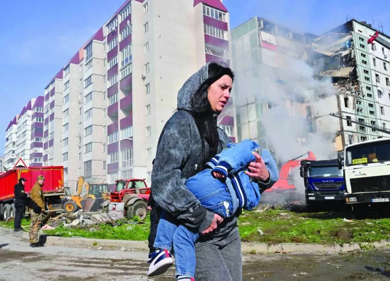 A woman carrying a child walks past damaged residential buildings in Uman.
