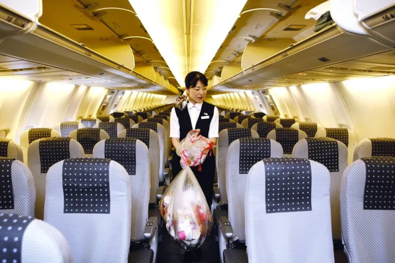 A cabin attendant carries bags of trash as she conducts her cleaning duties in the cabin of a Japan Airlines Co airplane at Haneda Airport in Tokyo (file). Handling cabin waste in airlines poses several challenges due to various factors such as limited storage capacity, weight and balance considerations and hazardous materials.