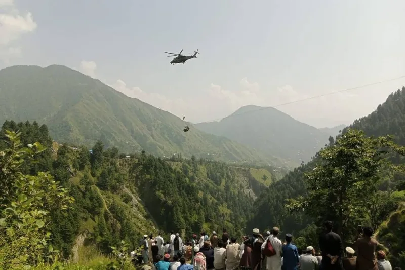 People watch as an army soldier slings down from a helicopter during a rescue mission to recover students stuck in a chairlift in Pashto village of mountainous Khyber Pakhtunkhwa province. AFP