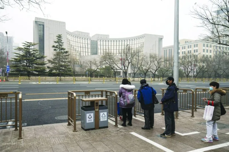 
Passengers wait at a bus stop across the People’s Bank of China building in Beijing. The central bank will trim the amount of foreign currency deposits banks are required to hold as reserves for the first time this year, the PBoC said yesterday. 