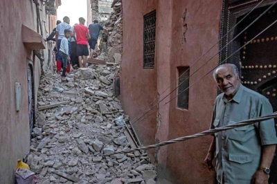 A man looks on as residents navigate through the rubble in the earthquake-damaged old city of Marrakesh on September 9, 2023. A powerful earthquake that shook Morocco late September 8 killed more than 600 people, interior ministry figures showed, sending terrified residents fleeing their homes in the middle of the night. (Photo by FADEL SENNA / AFP)