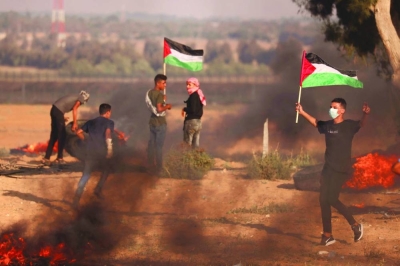 
Palestinian demonstrators carry the national flag during clashes with Israeli soldiers near the Israel-Gaza border fence, yesterday. 