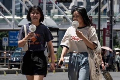 This photo taken on July 30, 2023 shows young women using portable fans to seek relief from the heat while walking outside Shinjuku station, as temperatures of 35C-plus (95F) have scorched the Japanese capital Tokyo for weeks. Selling jackets with in-built fans, neck coolers and T-shirts that feel cold, Japanese firms are tapping into a growing market for products to help people handle the summer heat. (Photo by Richard A. Brooks / AFP) / To go with AFP story Japan-weather-climate-technology-textile, FEATURE by Elie Guidi and Natsuko Fukue