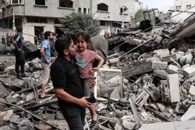 A man carries a crying child as he walks in front of a building destroyed in an Israeli air strike in Gaza City Saturday. AFP