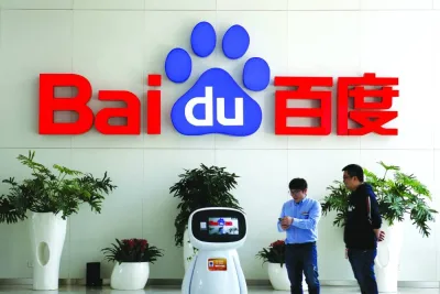 FILE PHOTO: Men interact with a Baidu AI robot near the company logo at its headquarters in Beijing.