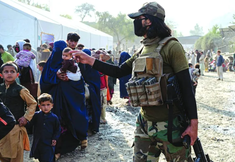 An Afghan security officer gestures as refugees arriving from Pakistan walk at the Afghanistan-Pakistan Torkham border in Nangarhar province.