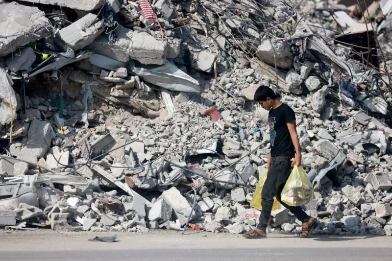 A youth carrying some belongings walks amid the rubble of destroyed buildings as people reach the central Gaza Strip via the Salah al-Din road on their way to the southern part of the Palestinian enclave on Sunday. AFP