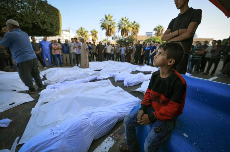 A Palestinian child sits next to the wrapped bodies of those killed in Israeli bombardment, prior to the corpses being taken from the Shuhada Al-Aqsa hospital for burial, in Deir el-Balah, in the central Gaza Strip on Tuesday. AFP