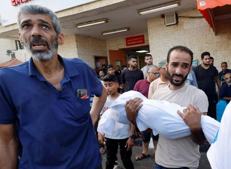 A Palestinian man carries the body a child killed in Israeli strikes at a hospital, in the central Gaza Strip, Sunday. REUTERS