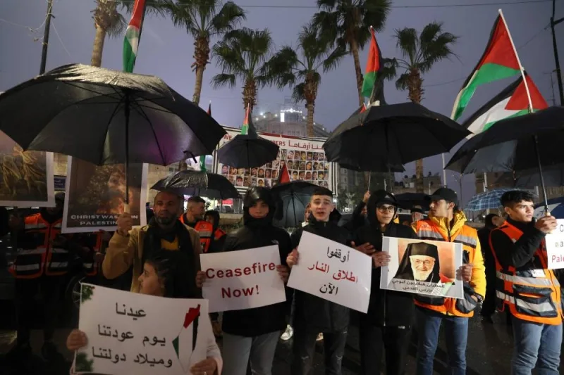 Palestinians lift placards and national flags during a protest in the rain in Ramallah in the Israeli-occupied West Bank  ahead of Christmas on on Saturday, demanding a ceasefire in Gaza. AFP