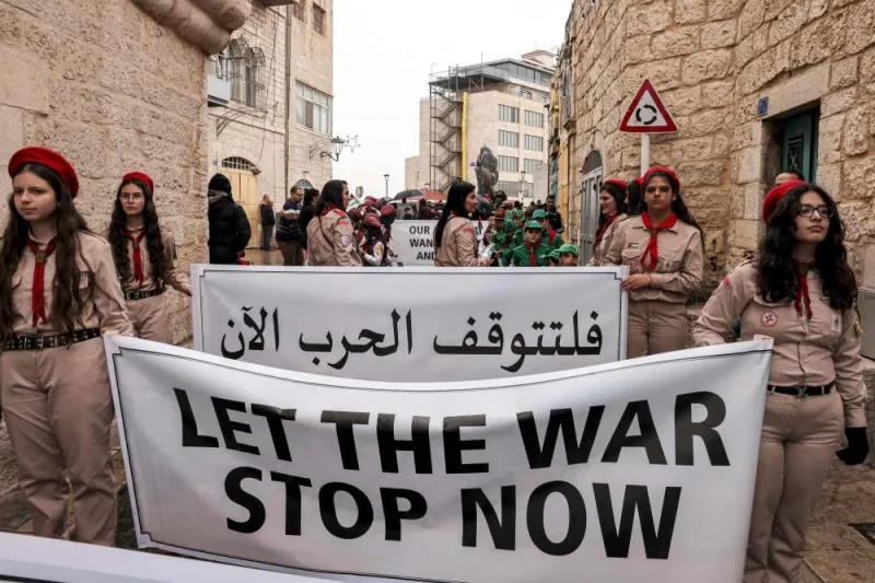 Palestinian youth members of the scouting movement hold up banners condemning and calling for an end of the conflict in the Gaza Strip during a procession welcoming the arrival of the Latin Patriarch of Jerusalem for Christmas Eve celebrations in the biblical city of Bethlehem in the occupied West Bank on Sunday.  AFP