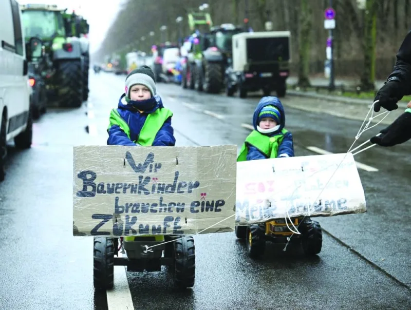 A farmers’ family with their children Jannik, 9, with a banner written “We farmers’ kids need a future” and Werner, 5, on mini tractors, from 
Fehrbellin, walk next to parked tractors on the street in front of the Berlin Victory Column in Berlin yesterday. (Reuters)