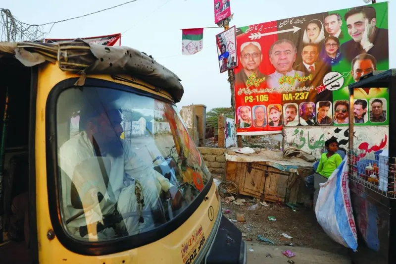 
A rickshaw driver waits for a customer while parked beside a campaign poster of a political party, ahead of general elections, in Karachi. 